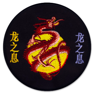 Ecusson rond brodé de club de judo. il représente un dragon rouge entourant une lune jaune au centre. A gauche et à droite, des idéogrammes jaunes et violet. le fond de l'écusson est noir.