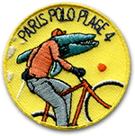 Ecusson rond brodé paris Polo plage. Il représente, sur un fond jaune, un crocodile à la veste orange et au pantalon gris faisant du vélo. le vélo est rouge, et au-dessus du dessin il est écrit en noir paris Polo Plage 4 en lettres capitales.
