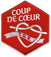 Ecusson brodé des Scouts et Guides de France (SGDF) du Tarn Quercy Rouergue en forme d'hexagone. Sur un fond rouge, le texte Coup de coeur est brodé en blanc sur le haut de la forme géométrique. Dessous, un coeur fait de deux lacets blancs se refermant avec au milieu, un bandeau sur lequel il est écrit TQR.