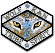 Ecusson du club de moto Wolf kan tran tribut. Il a une forme hexagonale et représente une tête de loup en très gros plan, les yeux jaunes ouverts. Autour, le nom du club de motards est inscrit en gris sur fond blanc.