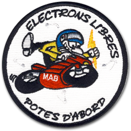 Ecusson rond brodé du club de moto des electrons libres. il représente un motard style cartoon avec un haut jaune et un casque bleu. Il enfourche une moto rouge sur laquelle il est écrit MAB. En haut et en bas de l'écusson, les textes suivants sont inscrits : electrons libres, potes d'abord, en noir sur fond blanc.