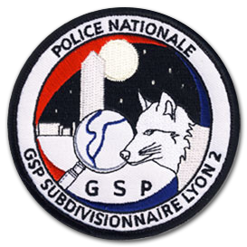 Ecusson rond brodé de la police nationale. Il représente un loup blanc de profil, à côté d'une loupe. Au fond, des bâtiments blancs sur un ciel étoilé au dessus duquel se trouve une lune. Le bord de l'écusson est blanc, il y est écrit police nationale GSP subdivisionnaire Lyon 2.
