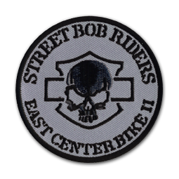 Ecusson rond brodé du club de moto des Street bob riders. Il a un fond gris, sur lequel une tête de mort noire est brodée devant une silhouette du logo harley davidson. Au bas de l'écusson, le texte east center bike II est écrit.