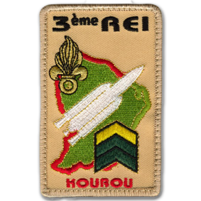 Ecusson brodé du 3ème régimerie étranger d'infanterie de Kourou, en Guyane. L'écusson est rectangulaire vertical. Il représente la forme de la Guyane en vert, sur laquelle sont brodés une fusée blanche et une grenade à 7 flammes, symbole de la légion étrangère. En haut, le texte 3ème REI est brodé en noir, et en bas, le texte kourou est brodé en rouge. Le tout est sur fond de toile beige.