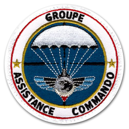 Ecusson militaire rond du groupe Assistance commando. L'écusson représente un parachute blanc ouvert, sur fond bleu. le texte Groupe assistance commando est brodé en noir sur fond blanc et bordé d'un fin cercle rouge.