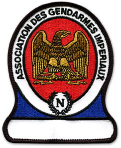 Ecusson brodé de l'association des gendarmes impériaux. Dans un ovale au bord blanc, il représente, sur un fond rouge, un aigle marron de face. Autour, le texte association des gendarmes impériaux est écrit en noir. L'ovale est posé sur un socle bleu et blanc.