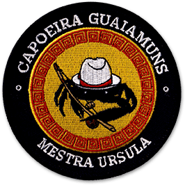 Ecusson brodé rond du club de capoeira Guaiamuns. Il représente au centre un scorpion avec un chapeau type panama sur fond jaune, borduré de rouge. Autour, un texte blanc sur fond noir : mestra ursula.
