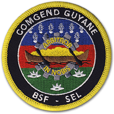Ecusson rond brodé de la gendarmerie de Guyane. Il représente une pirogue chargée marron et jaune sur fond bleu rouge vert. Sur le bord de l'écusson, en haut le texte COMGEND guyane, et en bas BSF - SEL.
