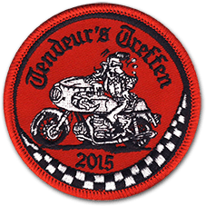Ecusson rond brodé de la concentration de motards Tendeur's Treffen de 2015, du club de moto des Tendeur's. L'écusson est brodé sur une toile rouge, en noir et blanc et représente un motard sur sa moto dans un style BD. En dessous, un damier noir et blanc.