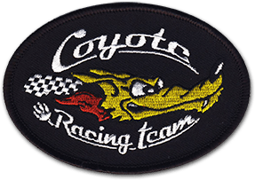 Ecusson de l'évènement journées Coyote. L'écusson brodé ovale a un fond noir sur lequel une tête de coyote est brodée, avec à sa gauche un damier noir et blanc. Au-dessus, il est écrit Coyote, et en-dessous racing team.