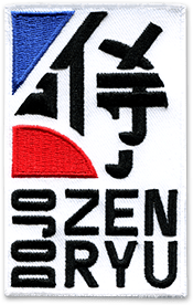 Ecusson brodé de forme rectangulaire vertical. Sur le partie haute, deux formes géométriques rouges et bleus et des idéogrammes chinois noirs. Dessous, en noir en lettres épaisses, le texte suivant est brodé : Dojo Zen Ryu, le nom du club d'arts martiaux.