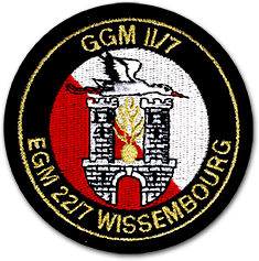 Ecusson rond brodé de l'escadron de gendarmerie mobile de Wissembourg. L'écusson a un fond rouge et blanc, sur lequel sont brodées les tours d'un chateau, une cigogne et la grenade à huit branches. Le contour est noir, brodé en lettres d'or EGM 22/7 Wissembourg.