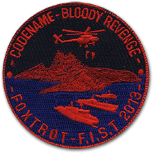 Ecusson rond brodé du club d'airsoft Foxtrot pour l'évènement foxtrot FIST 2013. Il représente, sur fond bleu et noir foncé, une ile rouge et des bateaux rouge survolées par un hélicoptère rouge. Au-dessus, le texte codename bloody revenge.