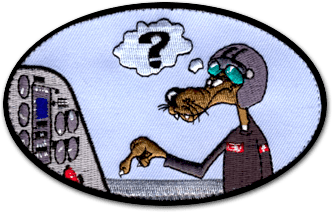 Ecusson de pilote d'avion de forme ovale horizontale. Il représente un chien, stype BD, avec un casque et des lunettes d'aviateur quis 'apprête à appuyer sur un bouton sur un tableau de bord de pilote d'avion. Au-dessus de la tête du chien, une bulle avec un point d'interrogation. Le fond de l'écusson est une toile bleu claire.