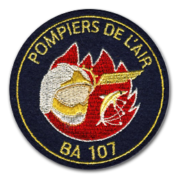 Ecusson rond brodé des pompiers de l'air. Au centre, une grande flamme rouge est recouverte par un casque de pompier gris et or et une silhouette de poisson. Dessus, le texte pompiers de l'air, et dessous, le texte BA 107 sont brodés en couleur or sur fond noir.