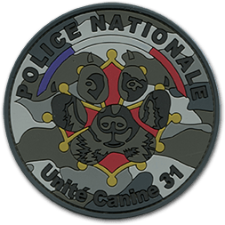 Ecusson rond PVC de l'unité canine de la Police nationale de Toulouse. Sur un fond camouflage, une tête de chien est représentée, entremêlée avec une croix occitane. Dessus, un fin bandeau bleau blanc rouge au-dessis duquel il est écrit en gris foncé police nationale. En bas de l'écusson, le texte unité canine 31.