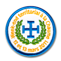 Ecusson rond brodé des scouts de Chaume. Sur fond blanc, au centre, est brodée en bleu une croix entourée de feuilles de laurier vertes. Autour, en jaune, le texte Weekend territorial à la Chaume 12 et 3 mars 2011 est brodé