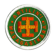 Ecusson rond brodé des scouts de Madagascar. Le fond est une toile verte sur laquelle est brodée au centre la croix scout en orange. Autour, un fin cercle blanc puis le texte Antilini, Madagasikara en orange.