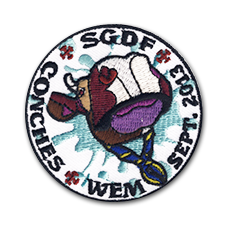 Ecusson brodé rond des scouts et guides de France de COnches. L'écusson représente une tête de vache en gros plan, avec un foulard scout noué autour du cou sur un find blanc et tâché de bleu. Sur le contour, il est écrit SGDF, Sept. 2013, WEM, Conches.