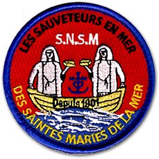 Ecusson des sauveteurs en mer des Saintes Marie de la Mer. L'écusson brodé représente deux sauveteurs sur un bateau, sur un fond rouge. Le texte SNSM est inscrit entre les deux sauveteurs.