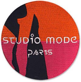 Ecusson brodé aux bords découpés portant le texte Studio mode Paris sur un fond rose et orange, avec des ombres noires.