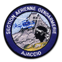 Ecusson rond brodé de la gendarmerie corse. il représente une montagne grise devant laquelle vole un hélicoptère bleu. Au premier plan du dessin, la tête de maure emblématique de la Corse est brodée. Le tour de l'écusson est un bandeau bleu foncé sur lequel le txte Section aérienne gendarmerie Ajaccio est brodé en blanc.