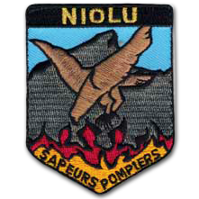 Ecusson brodé des sapeur pompiers de Niolu en Corse. il a une forme de balson en haut duquel se trouve une bande noire portant le texte couleur or Niolu. Sur l'écusson, un aigle au-dessus des flammes devant une montagne avec au bas, le texte Sapeurs pompiers.